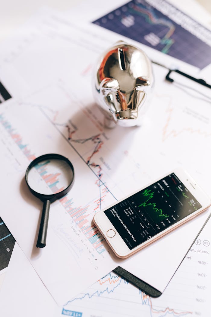 Smartphone displaying stock market, piggy bank, and magnifying glass on financial charts.