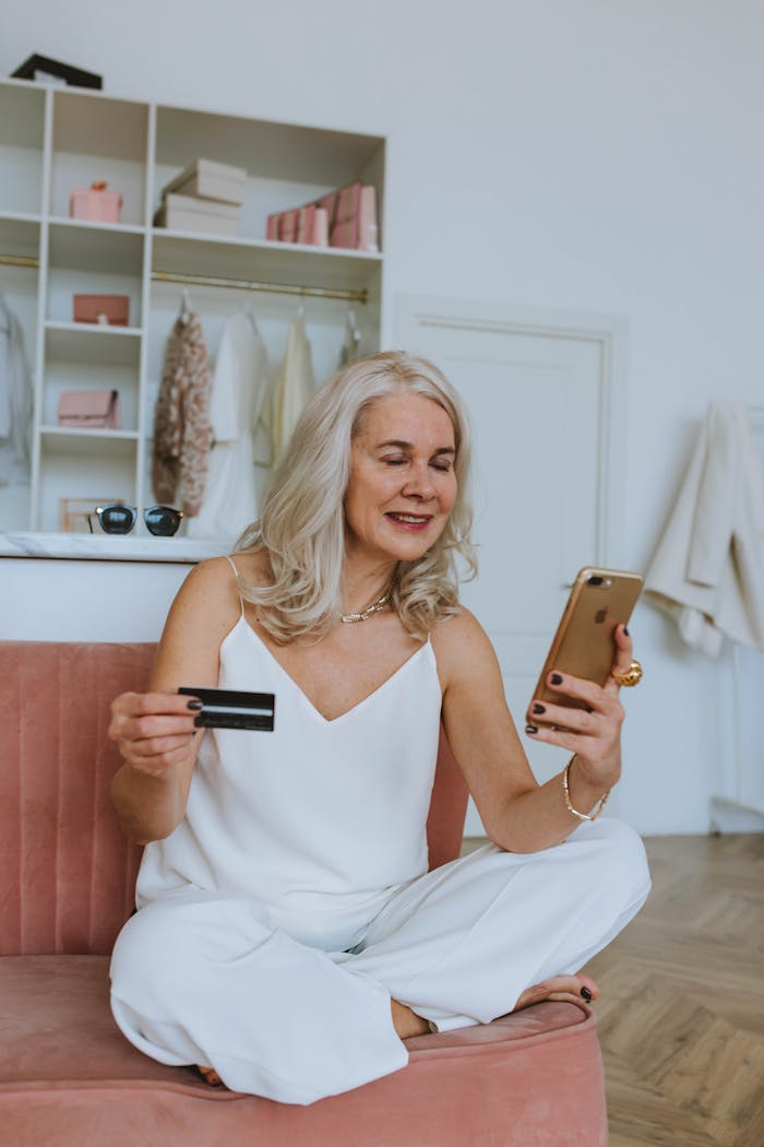 Services Elderly woman making online purchases with smartphone and credit card while sitting indoors.